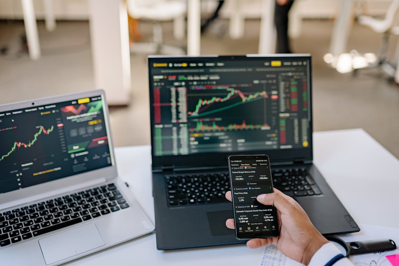 about-us-01 A professional tracks stock market trends using two laptops and a smartphone, showcasing digital finance tools.