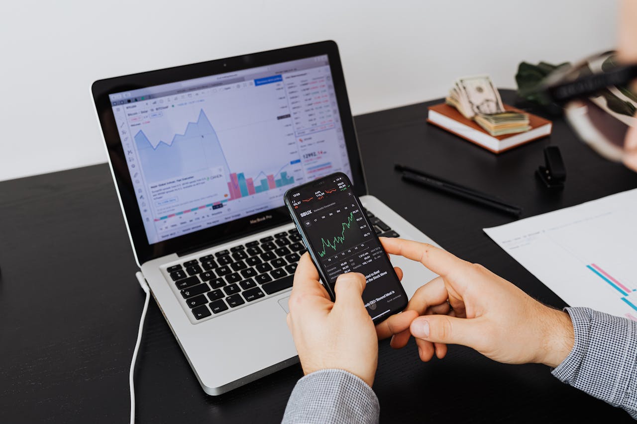 about-us-02 Person analyzing stock market data on a laptop and smartphone indoors.